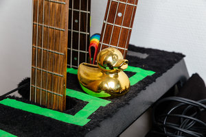 Eine goldene Badeente steht zwischen Gitarrenhälsen