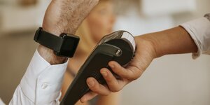Eine Person hält ihre Smartwatch an ein Bezahlgerät