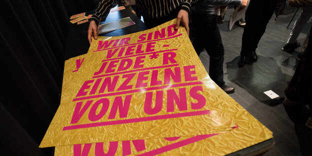Ein Plakat der Gruppe Die Vielen zeigt, auf einem Foto einer goldglänzenden Rettungsdecke in pinken Großbuchstaben den Slogan: "Wir sind viele - jede*r Einzelne von uns"