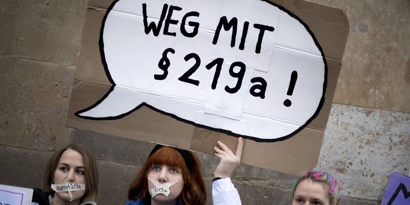 Junge Frauen, die ein Plakat mit der Aufschrft "Weg mit §219a" hochhalten