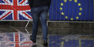 Die britische und die EU-Fahne hängen an einem Geländer, ein Passant spaziert daraufzu