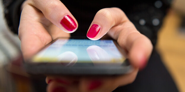 Eine Frau mit rot lackierten Fingernägeln hält ein Smartphone in der Hand