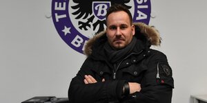Jens Redlich steht mit verschränkten Armen vor dem Wappen von Tennis Borussia Berlin
