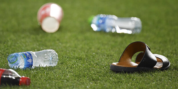 Plastiflaschen und eine Sandale liegen auf dem Rasen