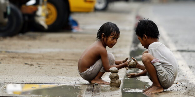 Zwei Kinder hocken am Straßenrand und spielen mit Schlamm