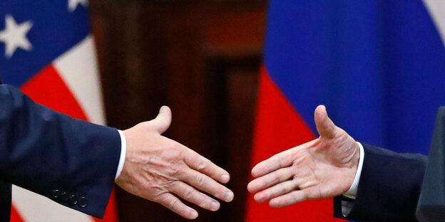 US Präsident Donald Trump (l) und der russische Präsident Wladimir Putin (r) geben sich die Hand. Im Hintergrund sind die Flaggen der USA und Russlands zu sehen