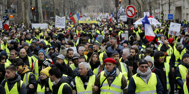 Eine Menschenmasse läuft durch Paris, alle tragen gelbe Westen und einige schwenken Frankreich-Fahnen