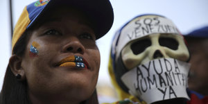 Eine Protestierende gegen Venezuelas Präsident Nicolás Maduroträgt ein Basecap und Lippenstift in den Farben der venezolanischen Flagge, neben ihr steht ein Demonstrant mit einer Totenkopfmaske