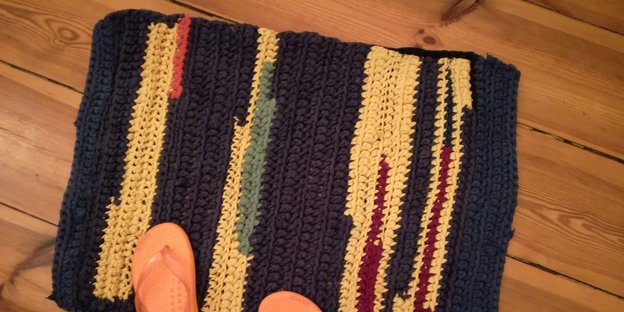 auf einem gehäkelten Badezimmerteppich, der auf Dielen liegt, stehen rosafarbene Flip-Flops auf einem gehäkelten Badezimmerteppich, der auf Dielen liegt, stehen rosafarbene Flip-Flops