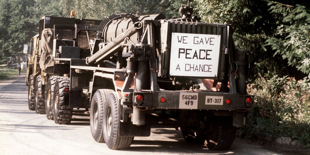 eine Rakete auf einem Armeelaster, hinten dran hängt ein Schild, auf dem „We gave peace a chance“ steht