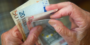 die Hände eines älteren Menschen halten mehrere Geldscheine