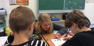 Eine junge Lehrerin hilft zwei Schülern in einem Klassenzimmer.