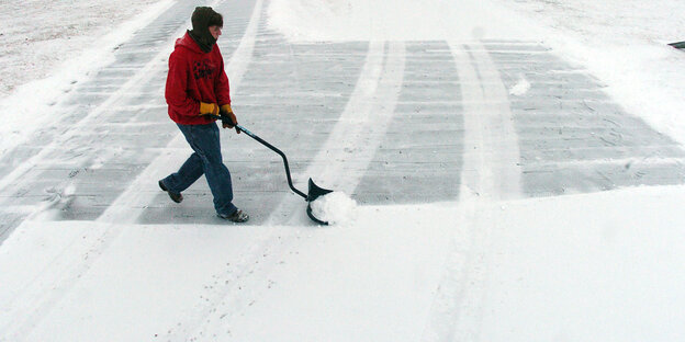 ein Mensch räumt mit einem Schneeschieber eine Straße