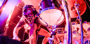 Ein Mann sitzt mit Maske vor einem Schlagzeug. Es ist der Drummer des US-Duos Lightning Bolt