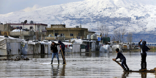 Flüchtlingszelte vor Gebäuden, im Hintergrund Berge, im Vordergrund Wasser