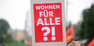 Eine Frau trägt ein Schild mit der Aufschrift "Wohnen fuer alle?!"