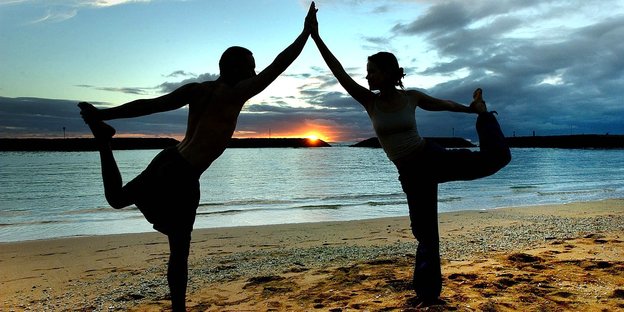 Zwei Menschen machen Yoga am Strand