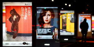 Beleuchtete Werbetafeln säumen einen Bürgersteig in Berlin, ganz vorne das aktuelle Plakat zur Berlinale