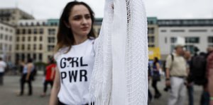 Eine Fraui trägt ein T-Shirt mit dem Aufdruck "GRL PWR" und hält ein weißes Kopftuch in der Hand