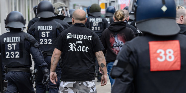 In Halle läuft ein Mann mit einem rassistischen Spruch auf dem Hemd zwischen Polizisten
