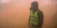 Ein vermummter Demonstrant der sogenannten "Gelbwesten" steht in dichtem Rauch von Rauchgranaten