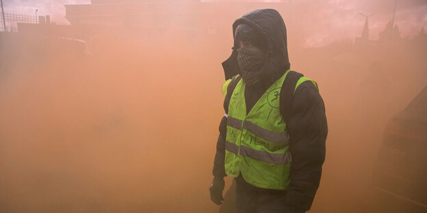 Ein vermummter Demonstrant der sogenannten "Gelbwesten" steht in dichtem Rauch von Rauchgranaten