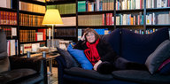 Eine Frau sitzt ausgestreckt auf einem Sofa, die Wände hinter ihr sind voller Bücher