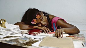 Eine Frau liegt mit ihrem Kopf auf einem Schreibtisch mit Dokumenten im ihrem Smartphone