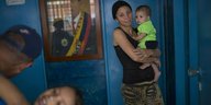 Vor einem Porträt von Hugo Chávez steht eine Frau, die ein Kind im Arm hält