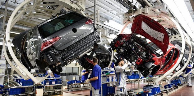 Zwei Autos hängen in einer Fabrik während Menschen an ihnen arbeiten