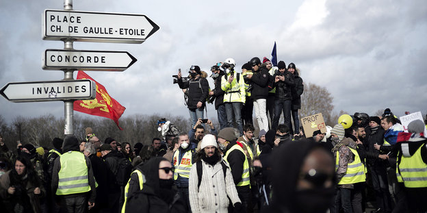 Viele Menschen, manche mit Gasmasken und maskiert - sie haben sich neben Pariser Straßenschildern versammelt