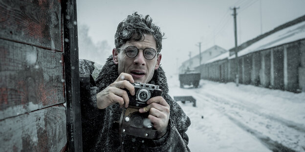 Ein Reporter mit Brille macht Fotos an einem verschneiten Bahnhof