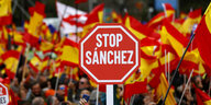 Vor zahlreichen spanischen Nationalflaggen wird ein Stoppschild mit der Aufschrift "Stop Sanchez" nach oben gehalten