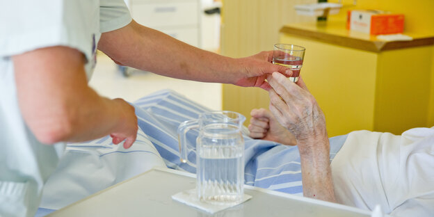 Eine Krankenpflegerin reicht einem Patienten ein Glas Wasser.