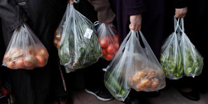 Menschen stehen in einer Schlange und halten Plastiktüten voll mit Gemüse