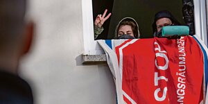 Zwei vermummte Jugendliche schauen aus einem Fenster und zeigen das Victory-Zeichen.
