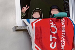 Zwei vermummte Jugendliche schauen aus einem Fenster und zeigen das Victory-Zeichen.