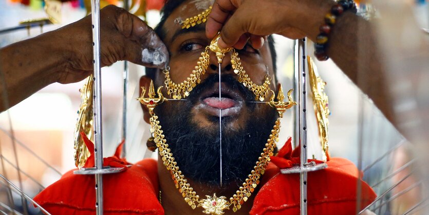 Ein Mann mit viel Schmuck hat eine Nadel durch seine Zunge gesteckt