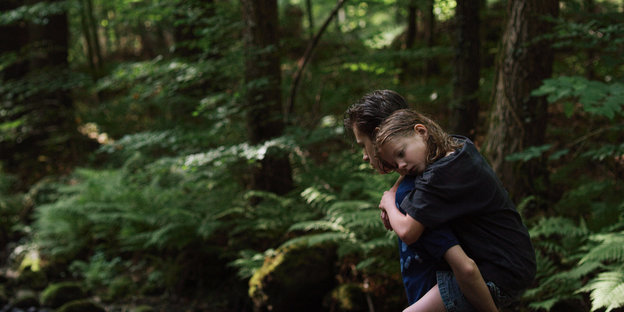 Ein Junge trägt seine jüngere Schwester auf dem Rücken durch den Wald