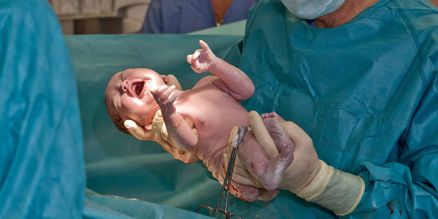 Ein Arzt hält ein neu geborenes Kind.