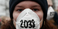 Ein Gesicht in Nahaufnahme mit weißer Atemschutzmaske, darauf ist die Zahl 2038 geschrieben