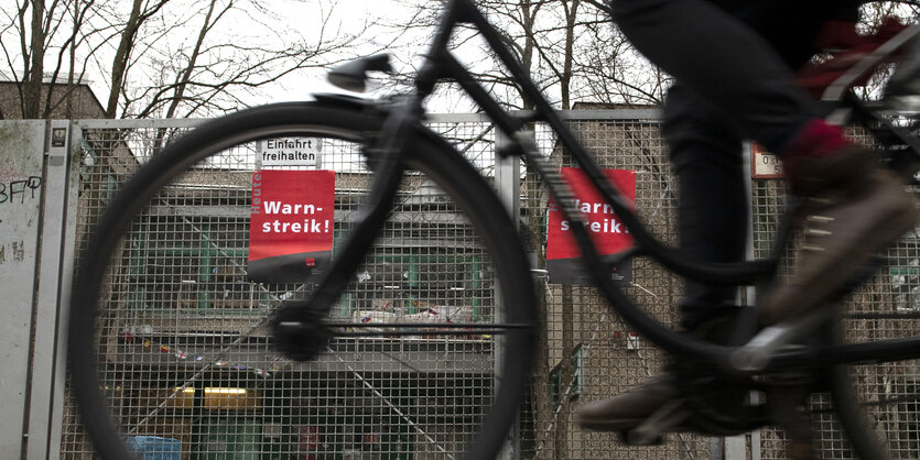 fahrrad fährt vorbei an verschlossener kindergartentür, an der ein schild hängt. darauf steht warnstreik