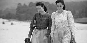 Zwei Frauen gehen an einem Strand entlang, die Szene ist in schwarz-weiß