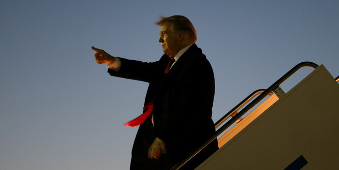 Trump steht auf der Gangway der Air Force one und zeigt mit dem Finge in die Ferne