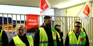 Drei Männer stehen in Warnwesten vor einem Zaun