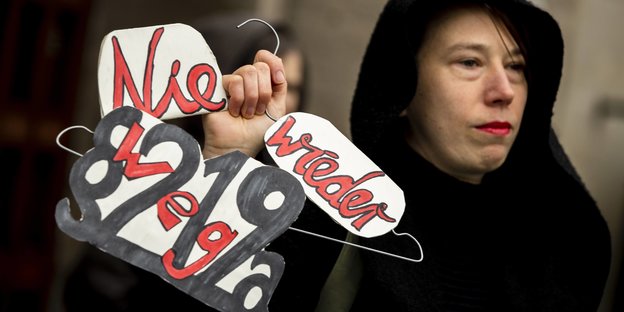 Eine Frau hält einen Kleiderbügel, auf dem ein Plakat mit der Aufschrift "Nie wieder Paragraf 219a" befestigt ist