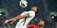 Zwei Fußballer,Augsburgs Reece Joel Oxford (l.) und David Alaba (Bayern München), springen zum Kopfballduell hoch