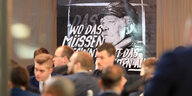 Männer in einem Sitzungssaal, auf einem großen Bild ist ein Foto von Bismarck zu sehen