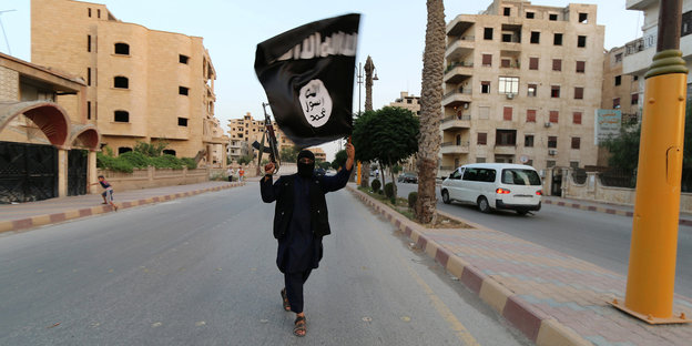 ein mensch läuft mit einer flagge des islamischen staates in den händen auf einer straße in raqqa, syrien