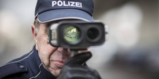 Mann mit Polizeimütze schaut durch eine Art Fernglas